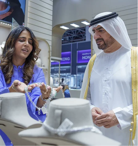 A man and a woman stand together in front of a jewelry display featuring watches and various jewelry pieces.